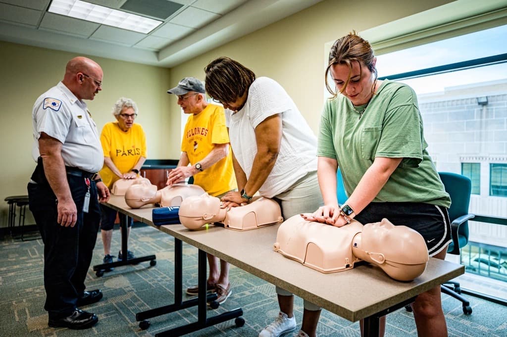 An EMS officer observing a community CPR class practising compressions on manikins.